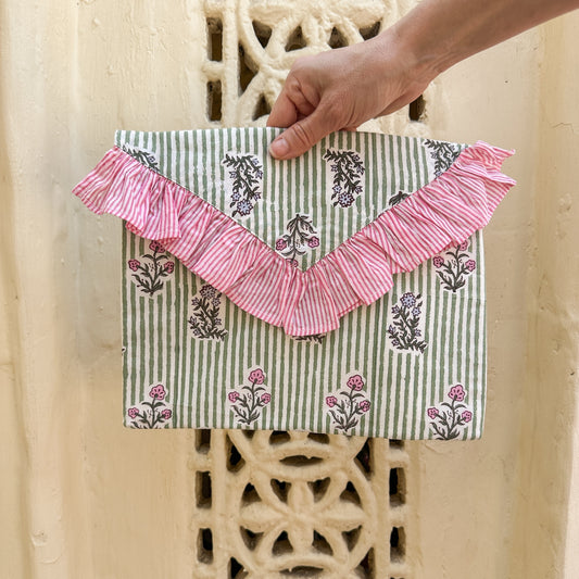 Clutch bag with pink ruffle and floral pattern held by a hand against a textured wall.